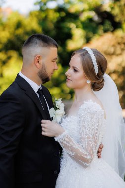 Bir gelin ve damat fotoğraf için poz veriyor. Gelin beyaz bir elbise ve saç bandı takıyor. Sahne mutlu ve romantik.