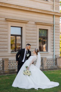 Bir gelin ve damat binanın önünde fotoğraf için poz veriyorlar. Gelin beyaz bir elbise giyiyor ve damat bir takım elbise giyiyor. Sahne mutlu ve kutlama dolu, çünkü çift evleniyor.