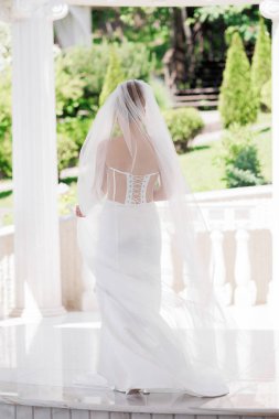 Beyaz bir duvak ve beyaz bir elbiseyle mermer bir zeminde bir gelin duruyor.