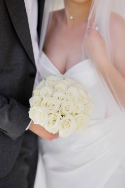 Bir gelin ve damat bir buket beyaz gül tutuyor. Gelin beyaz bir elbise giyiyor ve damat bir takım elbise giyiyor. Aşk ve mutluluk kavramı