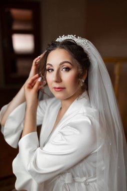 Beyaz bir elbise ve beyaz bir peçe takan bir kadın var. Bir sandalyede oturuyor ve kameraya bakıyor.