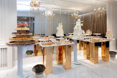 Beyaz masası ve altın masası olan büyük bir oda. Masada bir sürü pasta var.