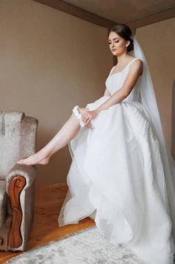 Bacak bacak üstüne atmış bir sandalyede oturan bir gelin ve beyaz bir gelinlik. Beyaz bir duvak ve beyaz bir alyans takıyor.