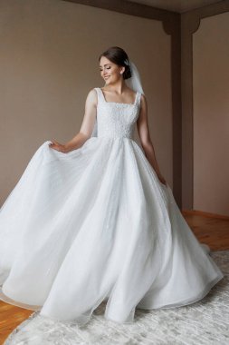 Beyaz gelinlikli bir kadın resim için poz veriyor. O bir peçe takıyor ve kollarını açıyor. İmajın mutlu ve kutlama havası var.