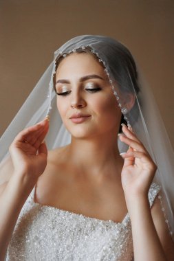 Bir kadın peçe takıyor ve elleri yüzünde. Beyaz bir elbise giyiyor ve saçları topuz şeklinde.