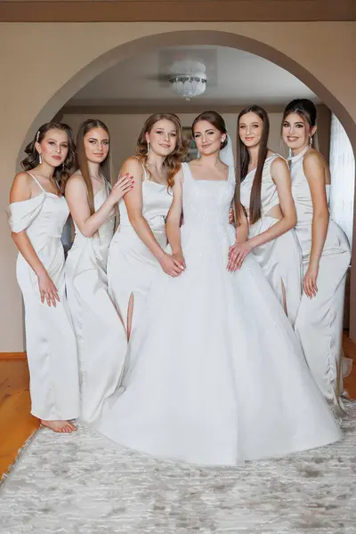 stock image A group of young women are posing for a picture in front of a bride's wedding dress. The bride is wearing a white gown and is surrounded by her five bridesmaids. Scene is joyful and celebratory