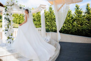 Beyaz elbiseli bir gelin merdivenlerden aşağı iniyor. Sahne beyaz kemerli ve gölgelikli bir bahçede geçiyor. Gelin peçe takıyor ve etrafı çiçeklerle çevrili.