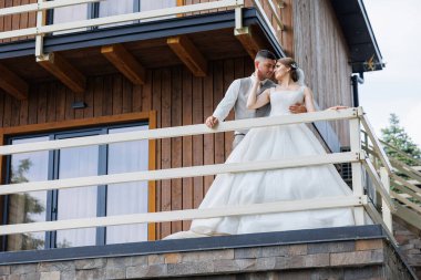 Bir gelin ve damat balkonda dikilip manzaraya bakıyorlar. Sahne romantik ve samimi, çünkü çift birbirini kucaklıyor ve birlikte olmaktan zevk alıyor.