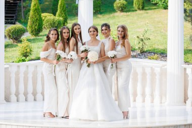 Beyaz elbiseli bir grup kadın beyaz bir kemer yolunun önünde fotoğraf için poz veriyor.