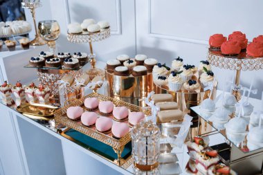 Pembe ve beyaz temalı tatlılarla dolu bir masa. Tatlılar tepsilerde sıralanır ve pek çok farklı pasta ve pasta çeşidi vardır.