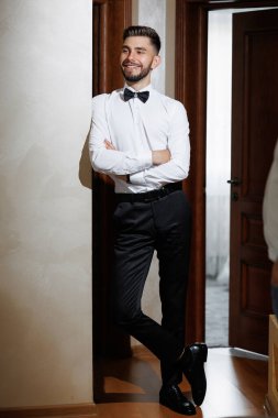 Takım elbiseli ve kravatlı bir adam kapının önünde duruyor. Gülümsüyor ve kendinden emin.