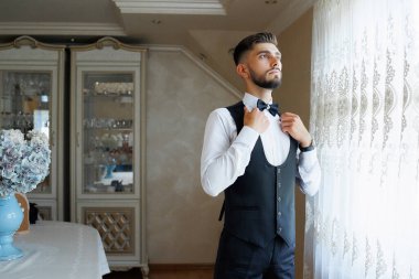 Takım elbiseli ve kravatlı bir adam pencerenin önünde kravatını düzeltiyor. Formalite ve profesyonellik kavramı. Çünkü adam takım elbise ve kravat giymiş.