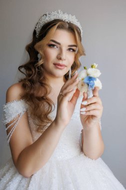 Bir kadın elinde bir çiçek tutuyor. Beyaz bir elbise ve taç giyiyor.