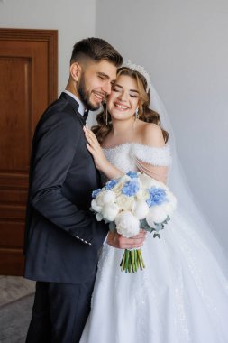 Bir gelin ve damat bir buket çiçekli fotoğraf için poz veriyorlar. Gelin beyaz bir elbise giyiyor ve damat bir takım elbise giyiyor. Sahne mutlu ve kutlama dolu.