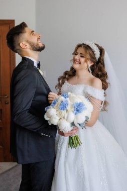 Bir gelin ve damat kameraya gülümsüyor. Gelin bir buket çiçek tutuyor ve damat bir buket çiçek tutuyor.