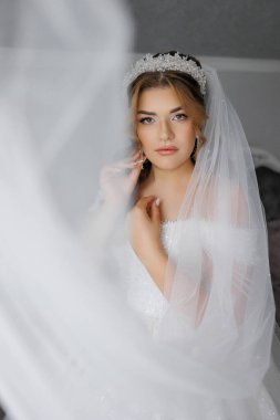 Beyaz bir duvak ve taç takan bir kadın var. Kameraya bakıyor.