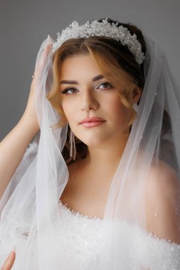 Beyaz duvak ve taç takan bir kadın. Gülümsüyor ve kameraya bakıyor.