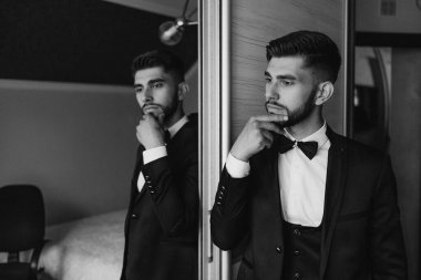 Takım elbiseli ve kravatlı bir adam aynanın önünde duruyor ve yansımasına bakıyor. Derin düşüncelere dalmış, muhtemelen kıyafetini ya da gününü düşünüyor. Formalite ve profesyonellik kavramı