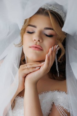 Bir kadın beyaz bir peçe takıyor ve başını ellerinin üzerinde dinlendiriyor. Yüzünde sakin bir ifade var.