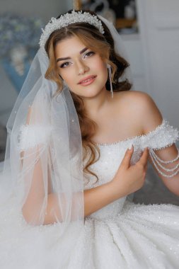 Beyaz gelinlik ve taç giyen bir kadın. Gülümsüyor ve kameraya bakıyor.