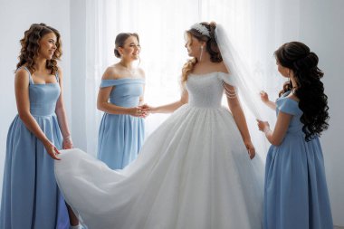 A bride is getting ready for her wedding with her bridesmaids. The bride is wearing a white dress and the bridesmaids are wearing blue dresses