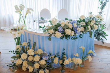 Üzerinde beyaz çiçekler ve mumlar olan mavi bir masa. Masa çiçekler ve mumlarla süslenmiş ve her iki tarafta iki sandalye var. Masa özel bir durum ve çiçekler için hazırlandı.