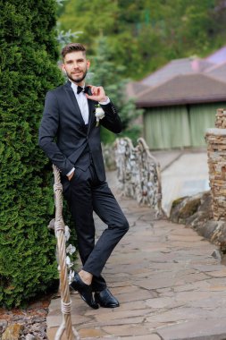 Takım elbiseli ve kravatlı bir adam taş kaldırımda duruyor. Gülümsüyor ve poz veriyor.