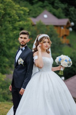 Gelin ve damat bir evin önünde duruyorlar, gelin bir buket tutuyor.