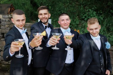 Takım elbiseli bir grup adam ellerinde şampanya kadehleriyle gülümsüyor. Sahne kutlama ve mutluluk dolu.