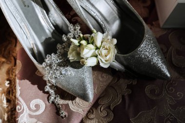 Üzerinde çiçek olan bir çift gümüş ayakkabı. Ayakkabılar pembe bir bezin üzerinde.