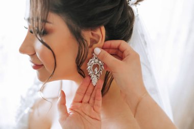 Bir kadın bir erkek tarafından kulaklarını deldiriyor. Kadın gelinlik giyiyor ve saçları topuz şeklinde.