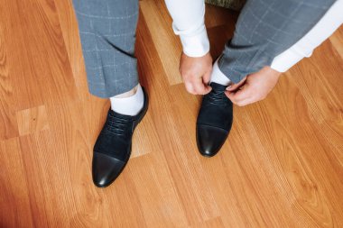 Bir adam ayakkabılarını giymeye hazırlanıyor. Gri bir takım elbise ve beyaz çoraplar giyiyor.