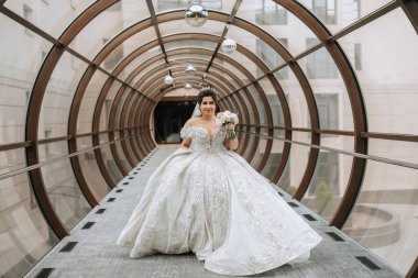 Uzun beyaz elbiseli bir kadın tünelde duruyor. Elinde bir buket çiçek tutuyor.