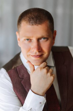 Takım elbiseli ve yelekli bir adam yüzünde bir gülümsemeyle kameraya bakıyor. O bir kravat ve bir yelek giyiyor ve onun saçı kısa. Güven ve profesyonellik kavramı