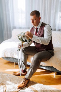 Takım elbiseli ve yelekli bir adam bir kanepede oturur, elinde bir buket çiçekle. Zarafet ve entelektüellik anlayışı, çünkü adam resmi giyinmiş.