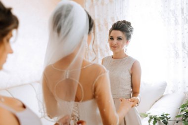 Bir gelin, annesi ve kız kardeşiyle evlenmeye hazırlanıyor. Gelin beyaz bir elbise ve duvak takıyor. Anne gelinin elini tutuyor ve kız kardeş de onların arkasında duruyor.