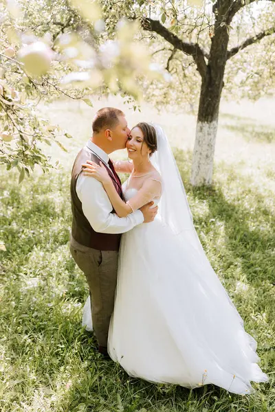 Bir gelin ve damat çimen tarlasında sarılıyorlar. Gelin beyaz bir elbise giyiyor ve damat yelek giyiyor.