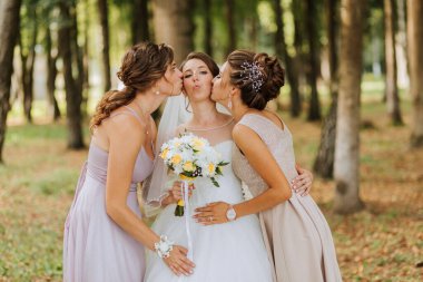 Üç kadın parkta sarılıp öpüşüyorlar. Bir tanesi gelinlik giyiyor.