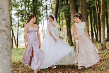 Gelinlik giymiş üç kadın ormanda yürüyor. Kadınlardan biri beyaz bir elbise ve duvak giyiyor.