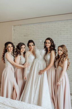 Beş kişilik bir grup beyaz bir duvarın önünde poz veriyor. Kadınlardan biri beyaz bir elbise giyiyor ve elinde bir şarap kadehi tutuyor. Diğer kadınlar da beyaz giyinmiş.