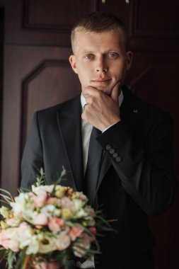 Takım elbiseli bir adam elinde bir buket çiçekle kapının önünde duruyor.
