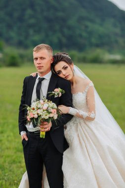 Bir gelin ve damat tarlada fotoğraf çektirmek için poz veriyorlar. Gelin beyaz bir elbise giyiyor ve damat da takım elbise giyiyor.