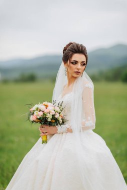 Bir gelin elinde bir buket çiçekle bir tarlada duruyor. Beyaz bir elbise ve duvak takıyor. Huzurlu ve huzurlu bir sahne, gelin uzaklara bakıyor.