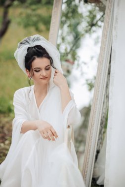 Beyaz elbiseli bir kadın aynanın önünde oturuyor. O bir peçe takıyor ve eli yüzünde. Huzurlu ve huzurlu bir sahne. Kadın dalgın dalgın bakıyor.