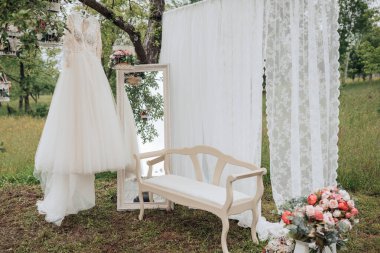 Beyaz bir elbise bir ağaç dalında asılı. Beyaz perdenin önünde beyaz bir bank var.