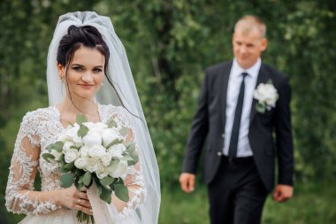 Bir gelin ve damat bir tarlada birlikte yürüyorlar. Gelin bir buket çiçek tutuyor ve damat takım elbise giyiyor. Sahne mutlu ve kutlama dolu, çünkü çift evleniyor.
