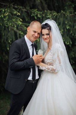 Bir gelin ve damat bir ağacın önünde fotoğraf için poz veriyorlar. Gelin beyaz bir elbise giyiyor ve damat da takım elbise giyiyor.