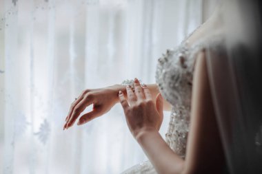 Bir kadın düğün için hazırlanıyor ve alyansını takıyor. Perdeli bir pencerenin önünde duruyor.