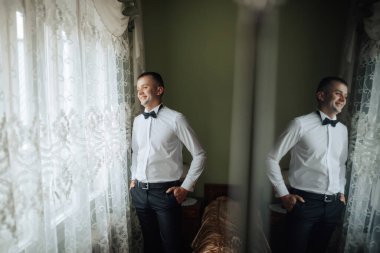 Takım elbiseli ve kravatlı bir adam pencerenin önünde duruyor, gülümsüyor. Güven ve mutluluk kavramı, adam anın tadını çıkarırken. Penceredeki yansıma zarafet katıyor.