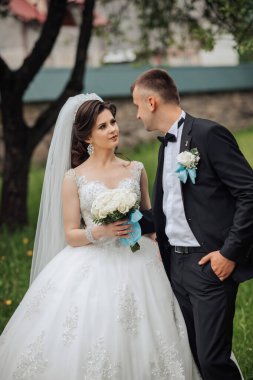 Gelin ve damat bir tarlada, gelin bir buket çiçek tutuyor. Sahne mutlu ve romantik, çift düğünlerini kutlamaya hazırlanıyor.
